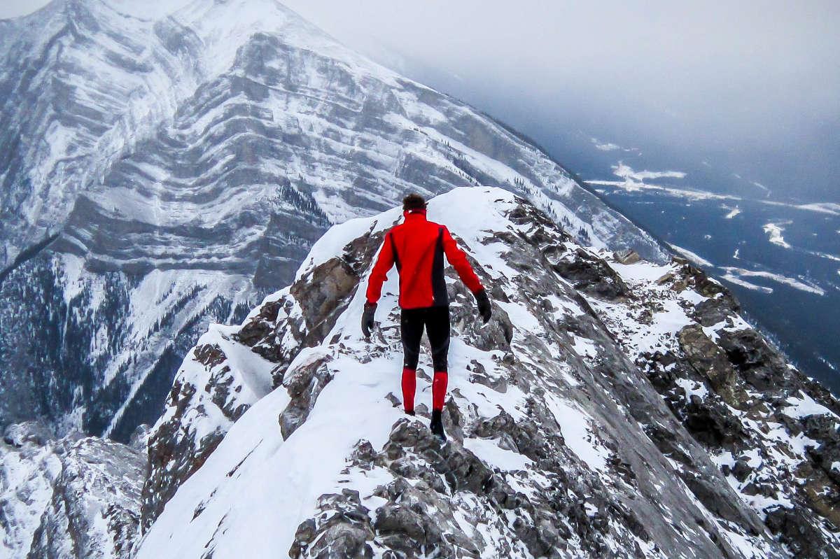 Ein Bergläufer in rot-schwarzem Lauf-Outfit überquert vorsichtig einen schneebedeckten Gebirgspass.